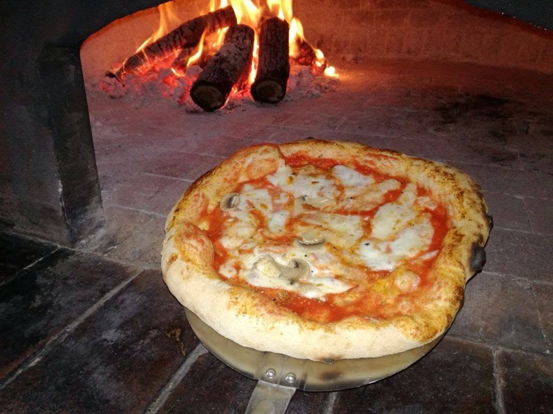 Pizza con pomodoro, mozzarella e funghi su pala di metallo nel forno a legna acceso di Al 76 da Michele
