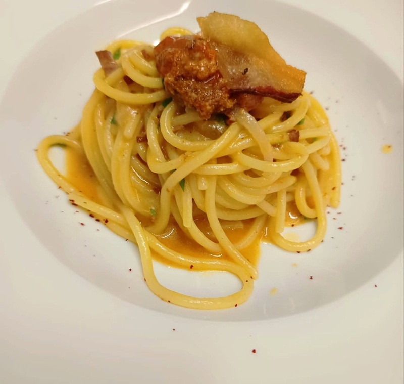 Spaghetti in nido con sugo arancio, guanciale croccante e polvere di peperoncino in un piatto fondo bianco