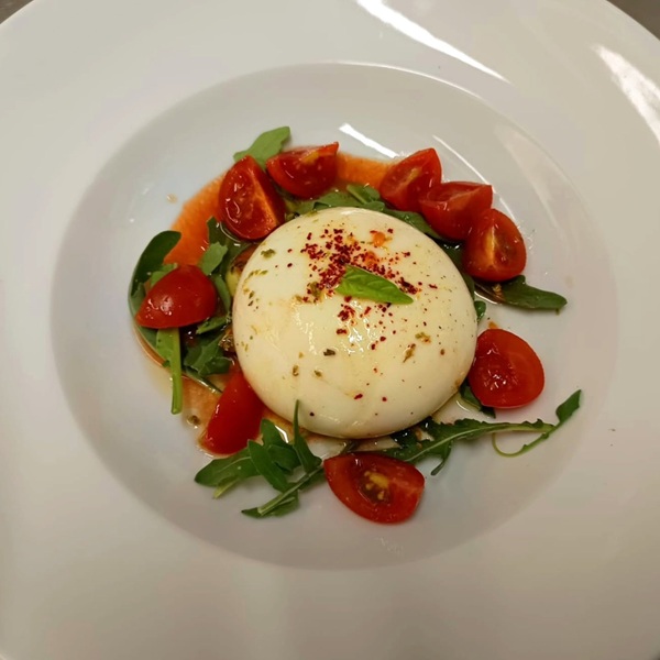 Burrata su rucola, pomodorini tagliati, peperoncino a scaglie e una foglia di basilico nel piatto bianco di Al 76 da Michele